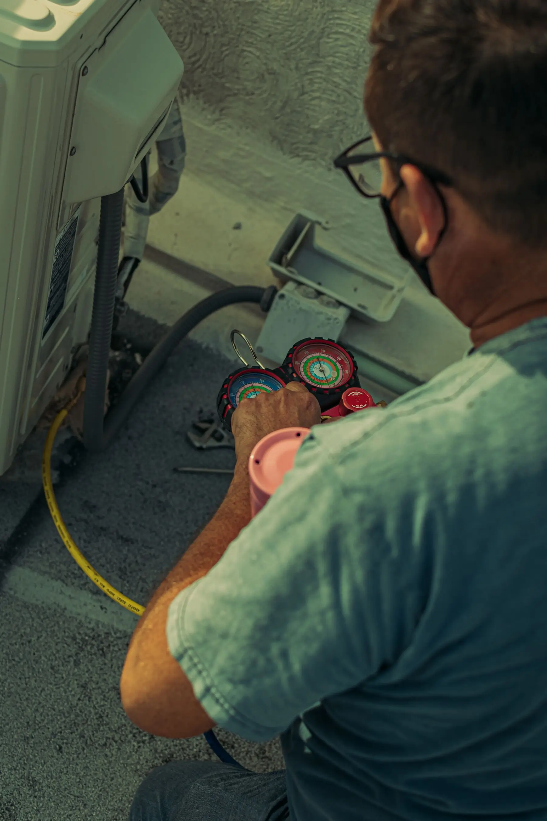 A technician holding refrigerant gauges at an outdoor condenser